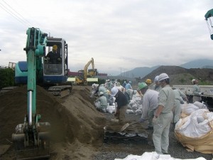 ﾊﾞｯｸﾎｳのそばでは、各社の従業員が土のう作成器に投入された砂をｽｺｯﾌﾟで一定量に整えていきます。